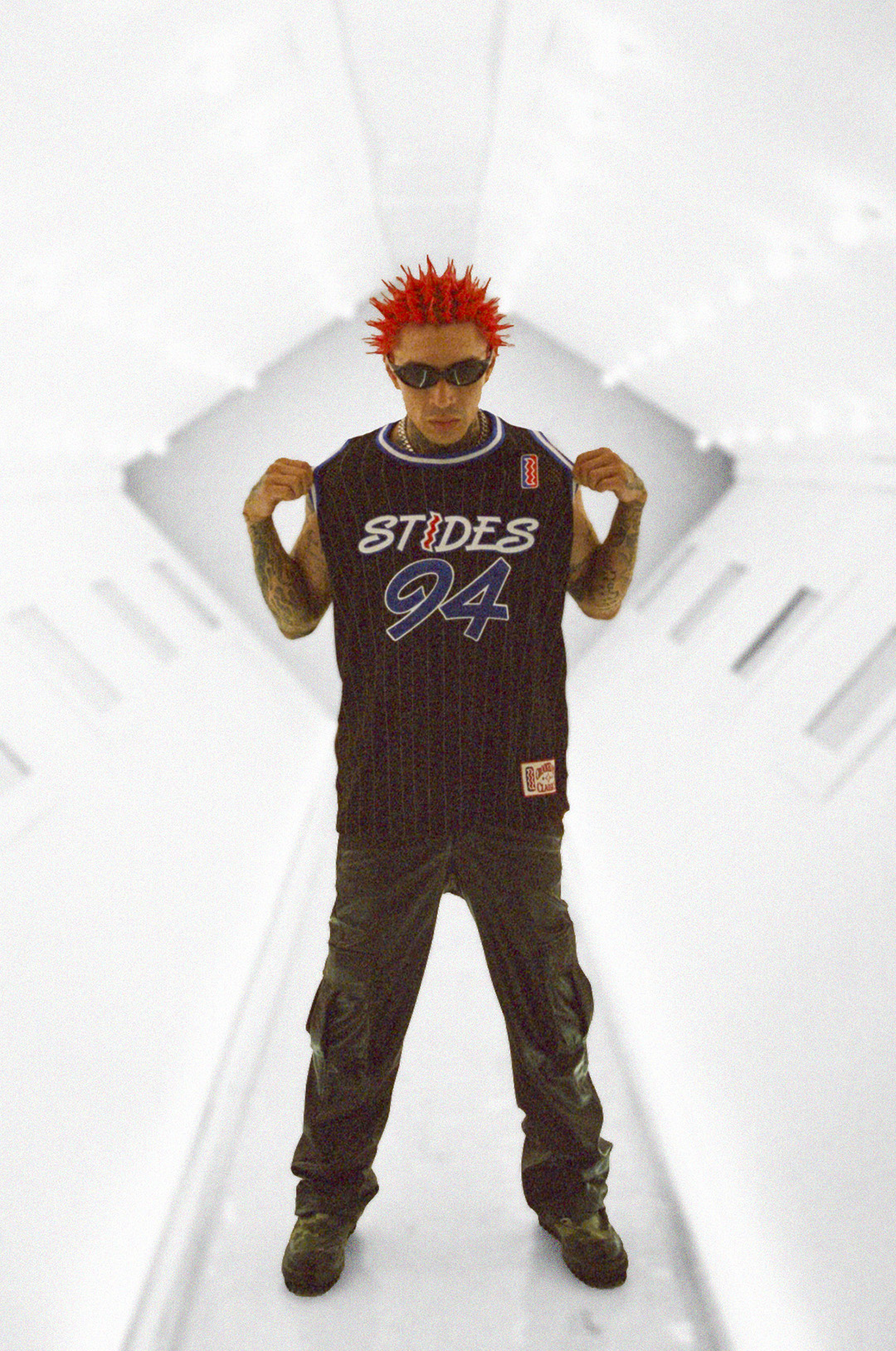 A person with red spiky hair and sunglasses wears a basketball jersey in a white hallway.