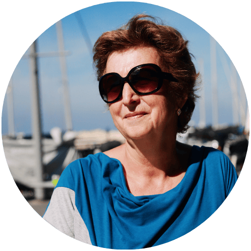 Person wearing sunglasses and blue shirt, standing outdoors with boats in background.