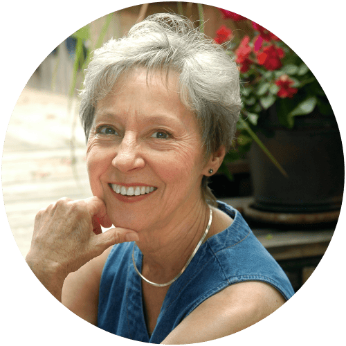 Smiling woman with short gray hair outdoors, wearing a blue sleeveless top.