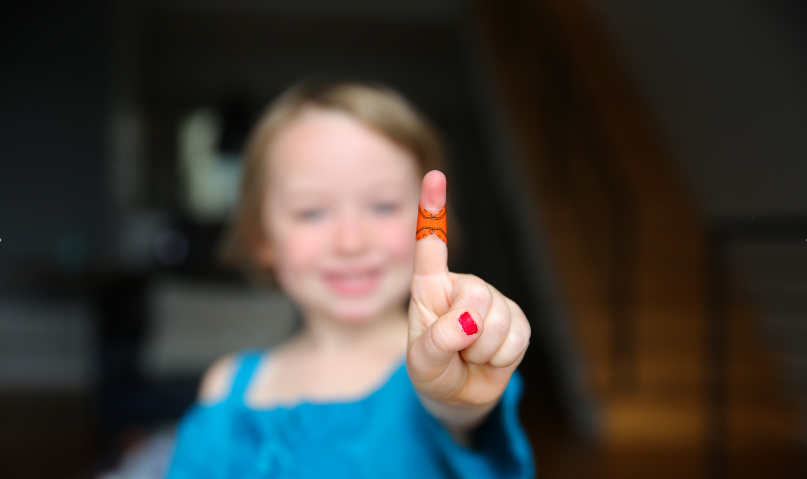 Child smiling, pointing with a bandaged finger and red nail polish.