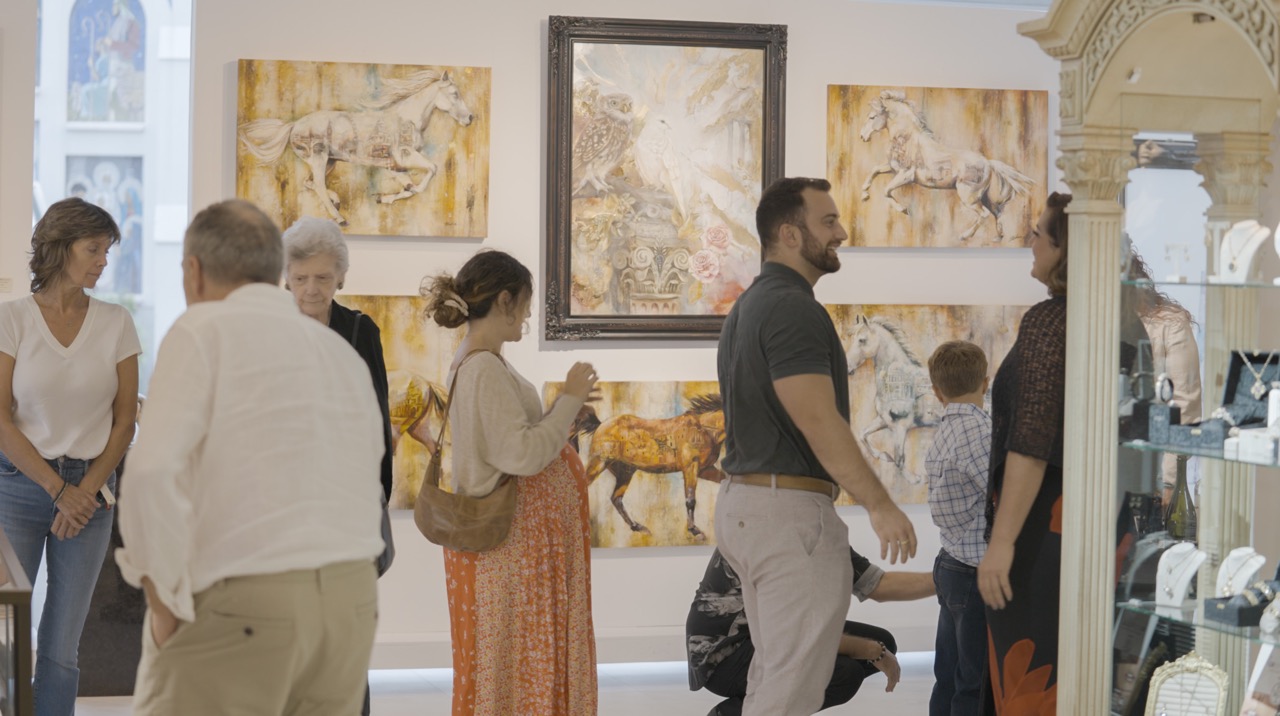 People viewing artwork in a gallery, horse paintings displayed on the walls.