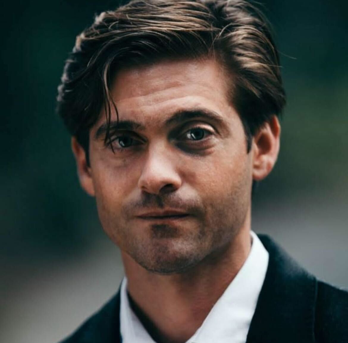 Man with brown hair in a suit looking directly at the camera.