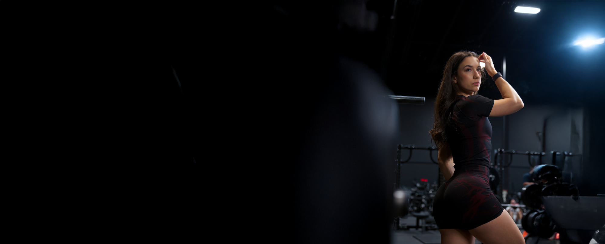 A woman in workout clothes looks over her shoulder in a dimly lit gym.