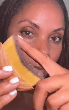 A close-up of a woman with dreadlocks holding a yellow bar of soap in a paper wrapper.