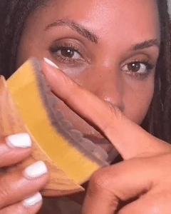 A person holds a yellow and clear cosmetic patch close to their eye.
