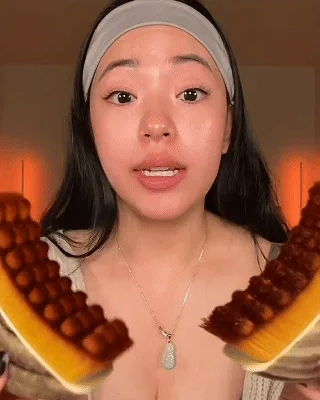 A woman with a headband holds two halves of a pastry with round, brown toppings towards the camera.