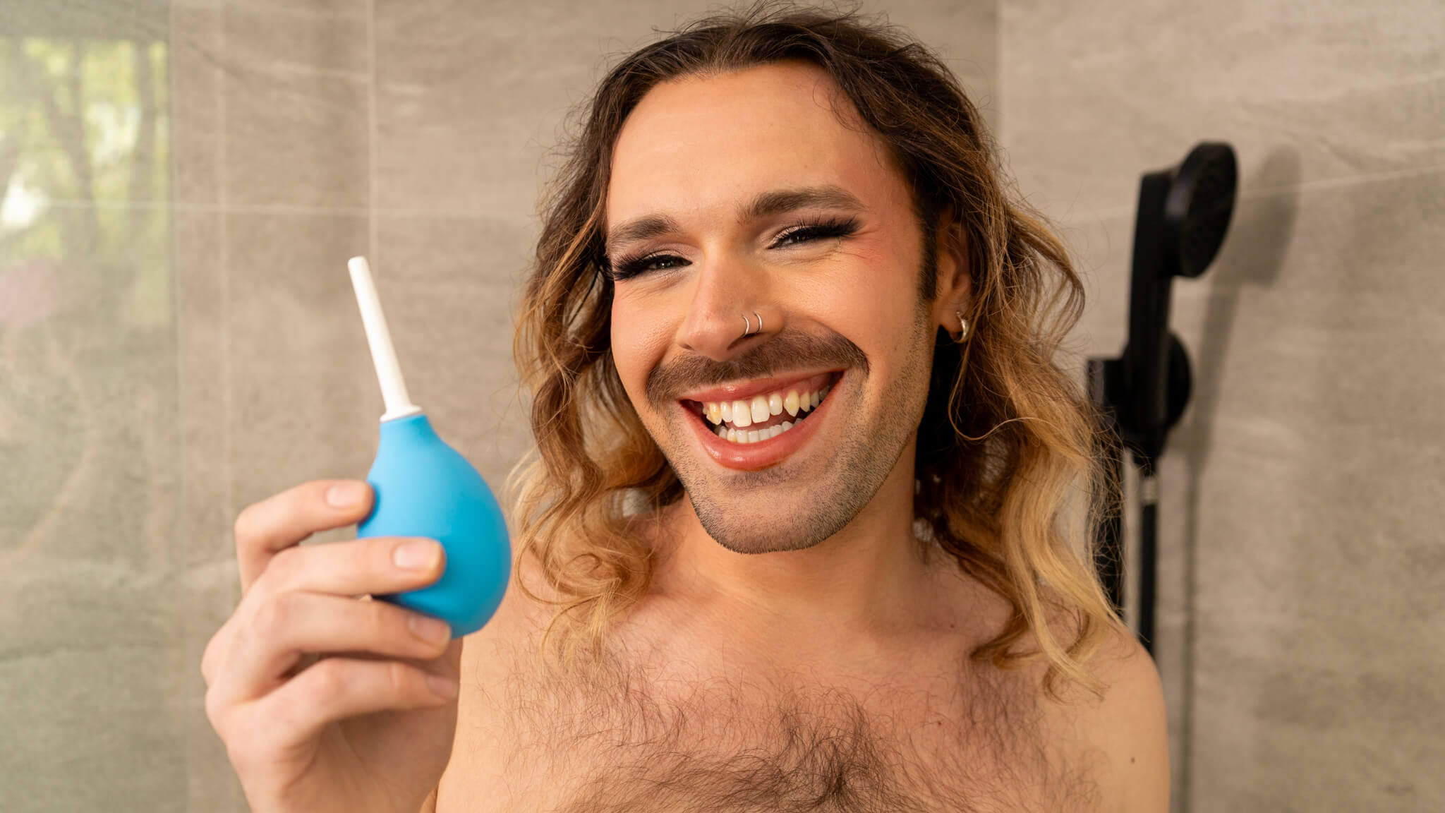 Person smiling, holding a blue enema bulb in a bathroom.