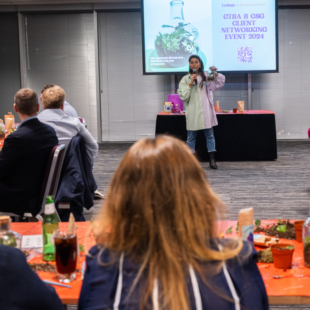Woman speaking at a networking event with attendees seated at tables.