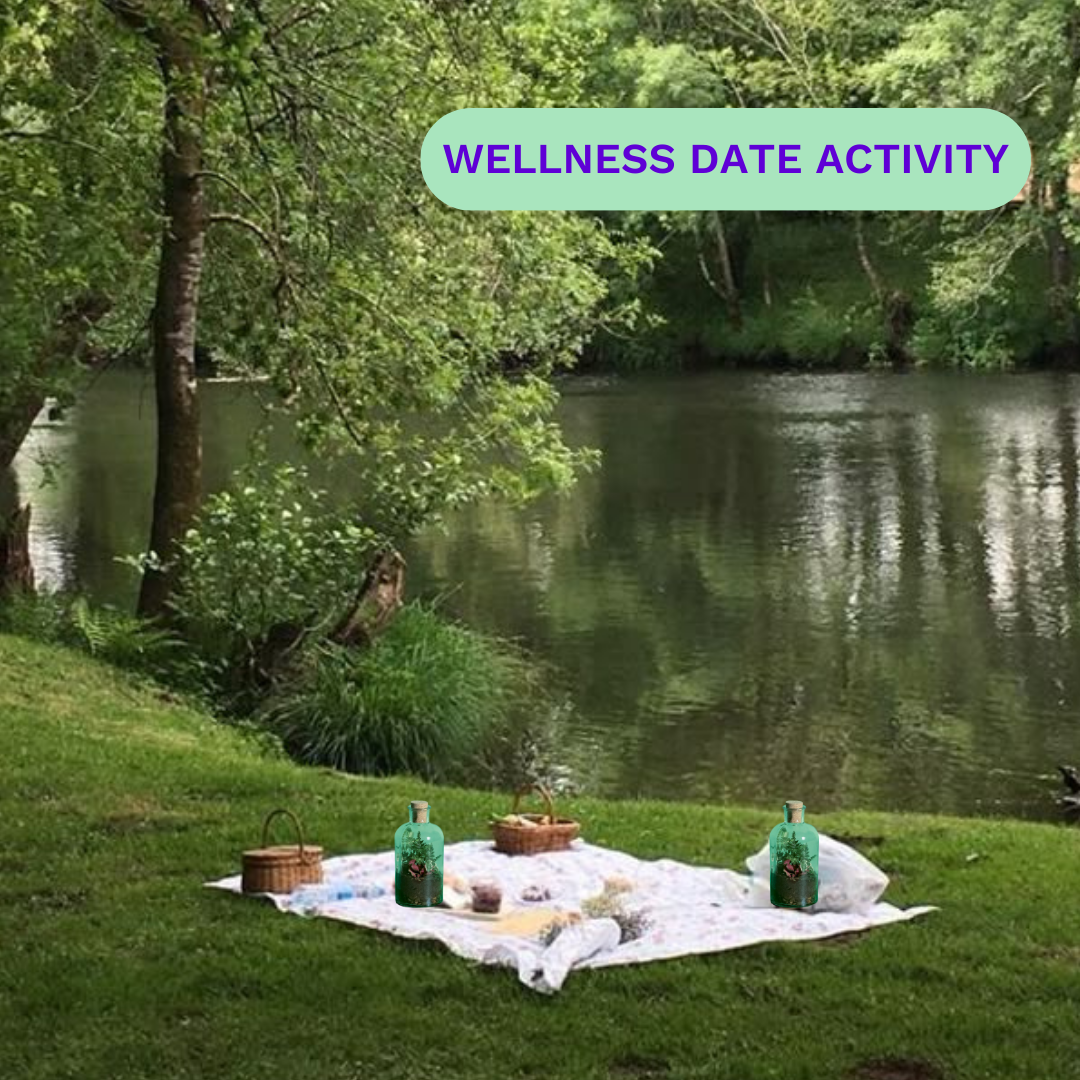 Picnic setup by a river with baskets and bottles on a blanket.