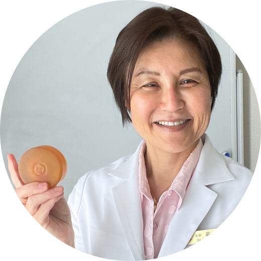 Person in a white coat holding a round, orange object, smiling.