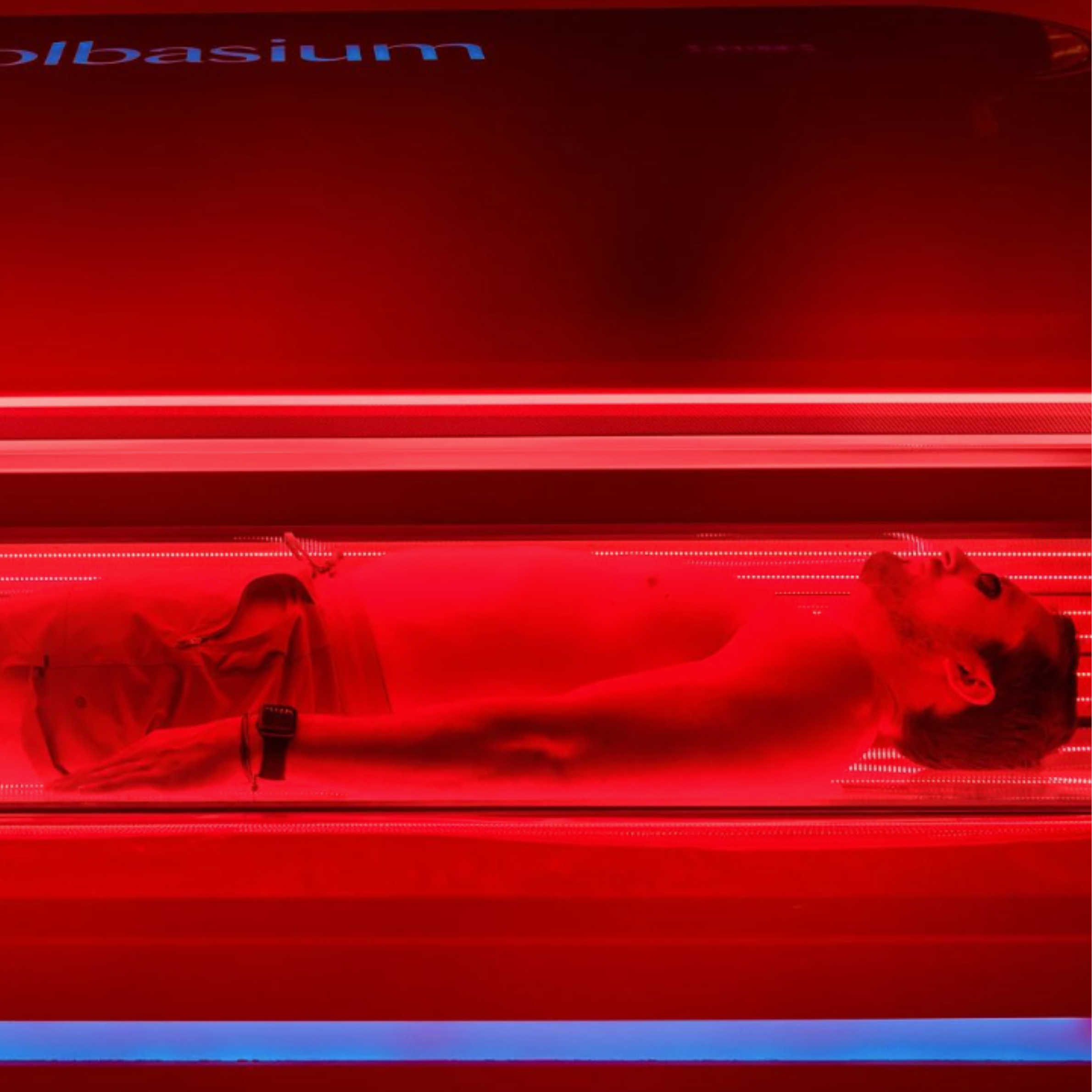 Person lying in a red-lit tanning bed.