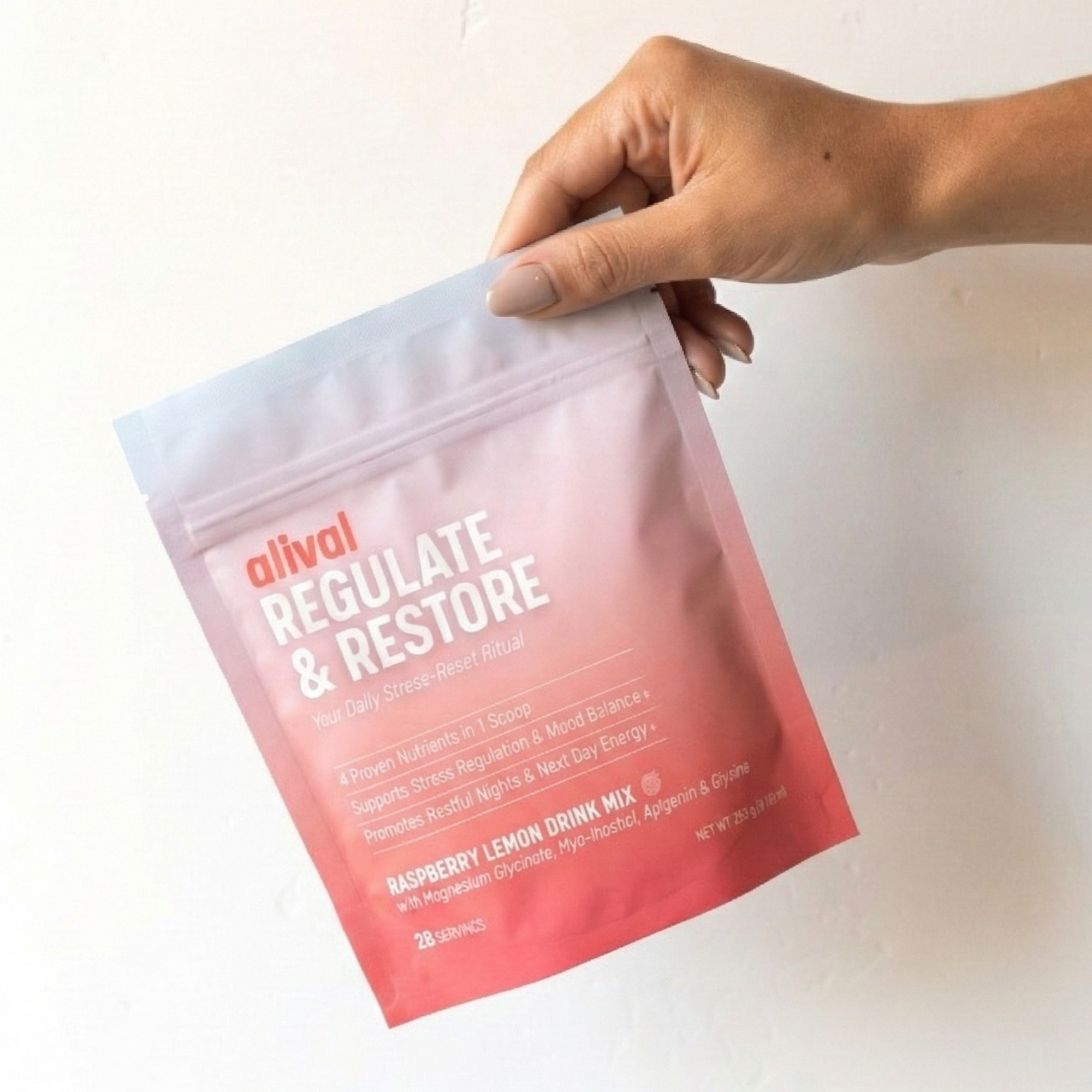 Hand holding a pink pouch labeled 'Regulate & Restore' raspberry lemon drink mix.