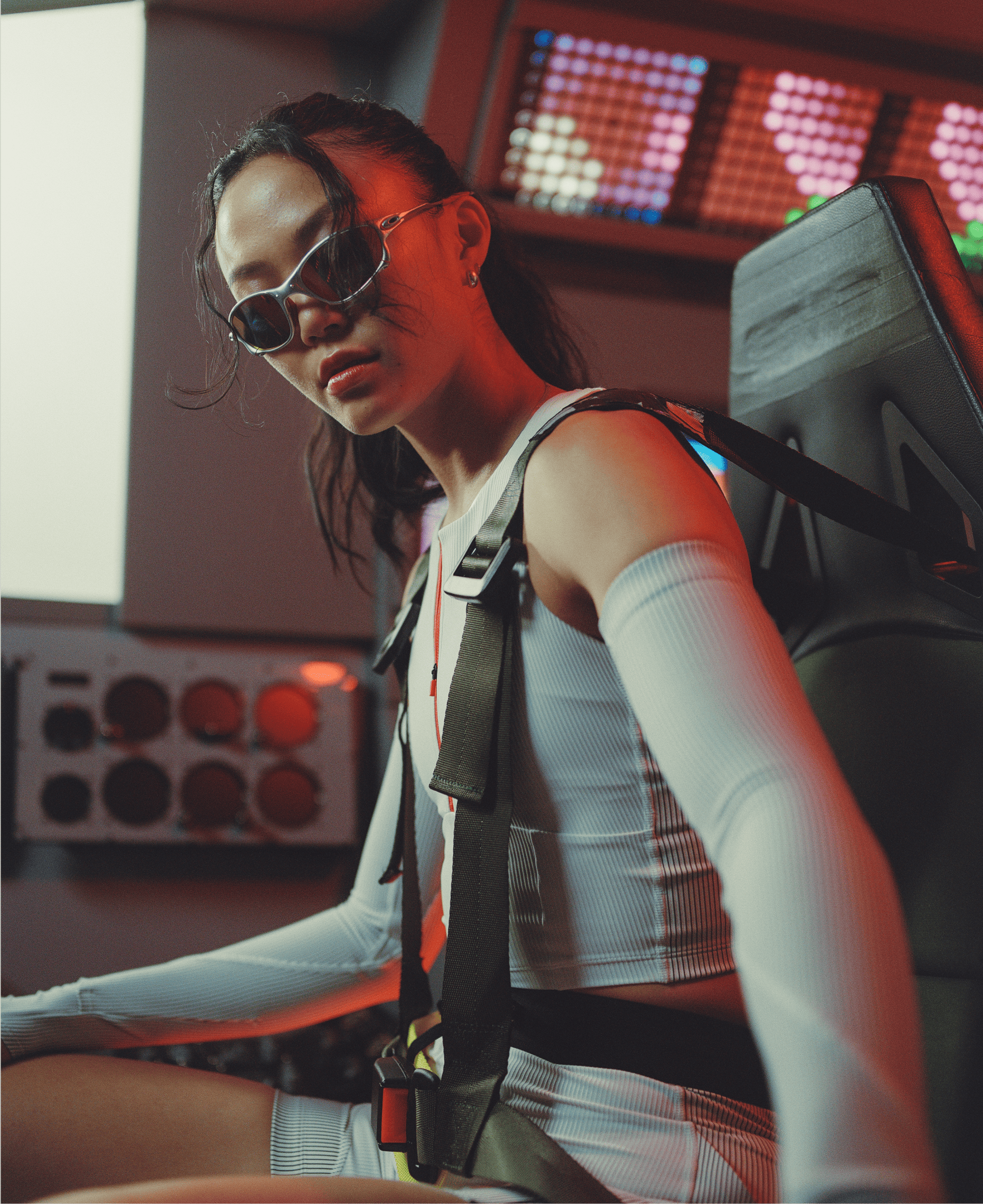 Person in futuristic setting wearing sunglasses and harness, with colorful lights in the background.