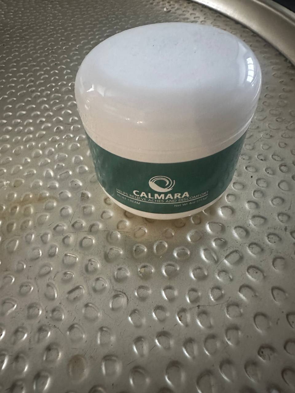 A jar of cream labeled 'Calmara' on a textured metal surface.