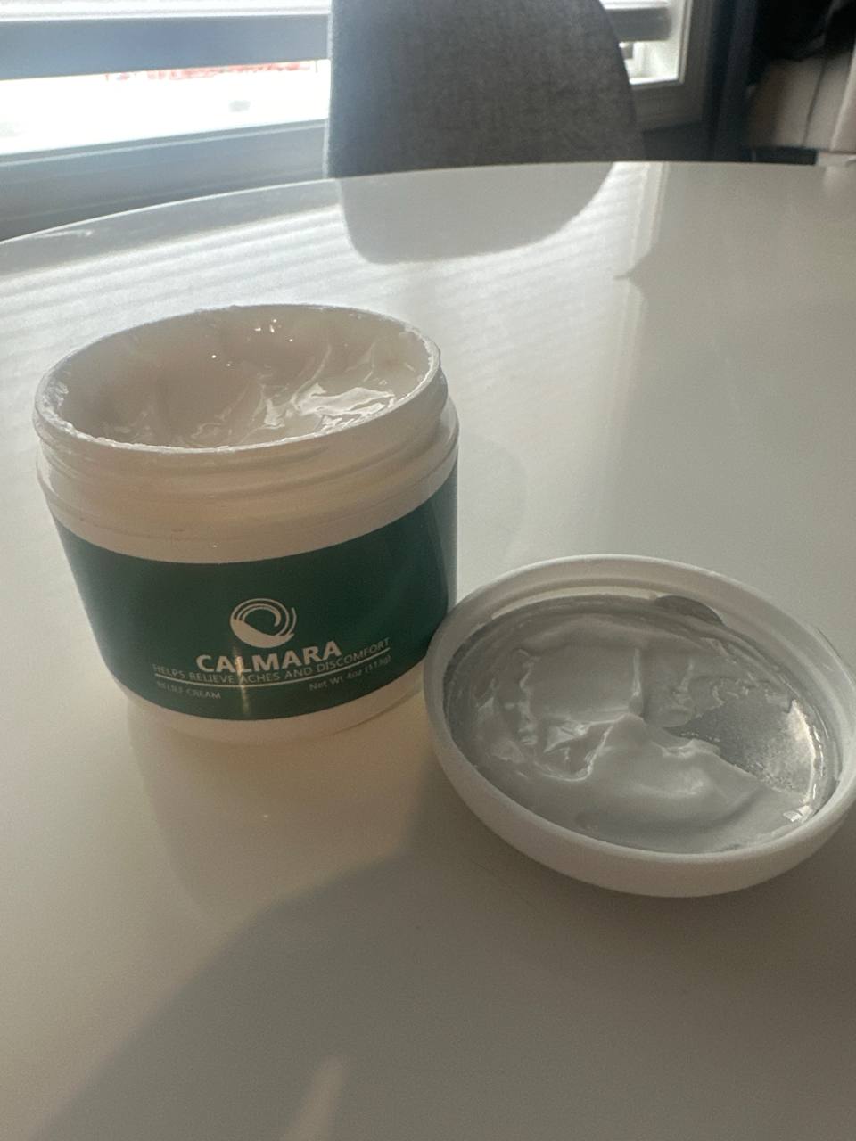 Open jar of cream labeled 'Calmara' on a white table.