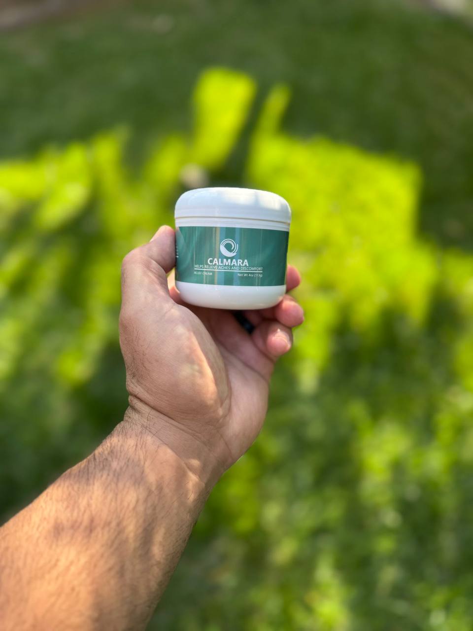 Hand holding a jar labeled 'Calmara' against a blurred green background.