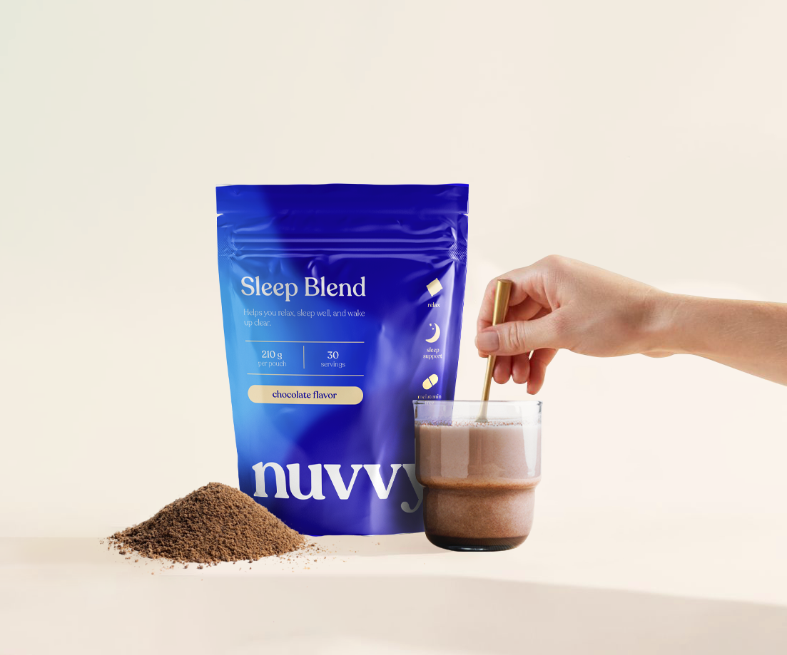Hand stirring chocolate drink beside a blue Sleep Blend pouch.