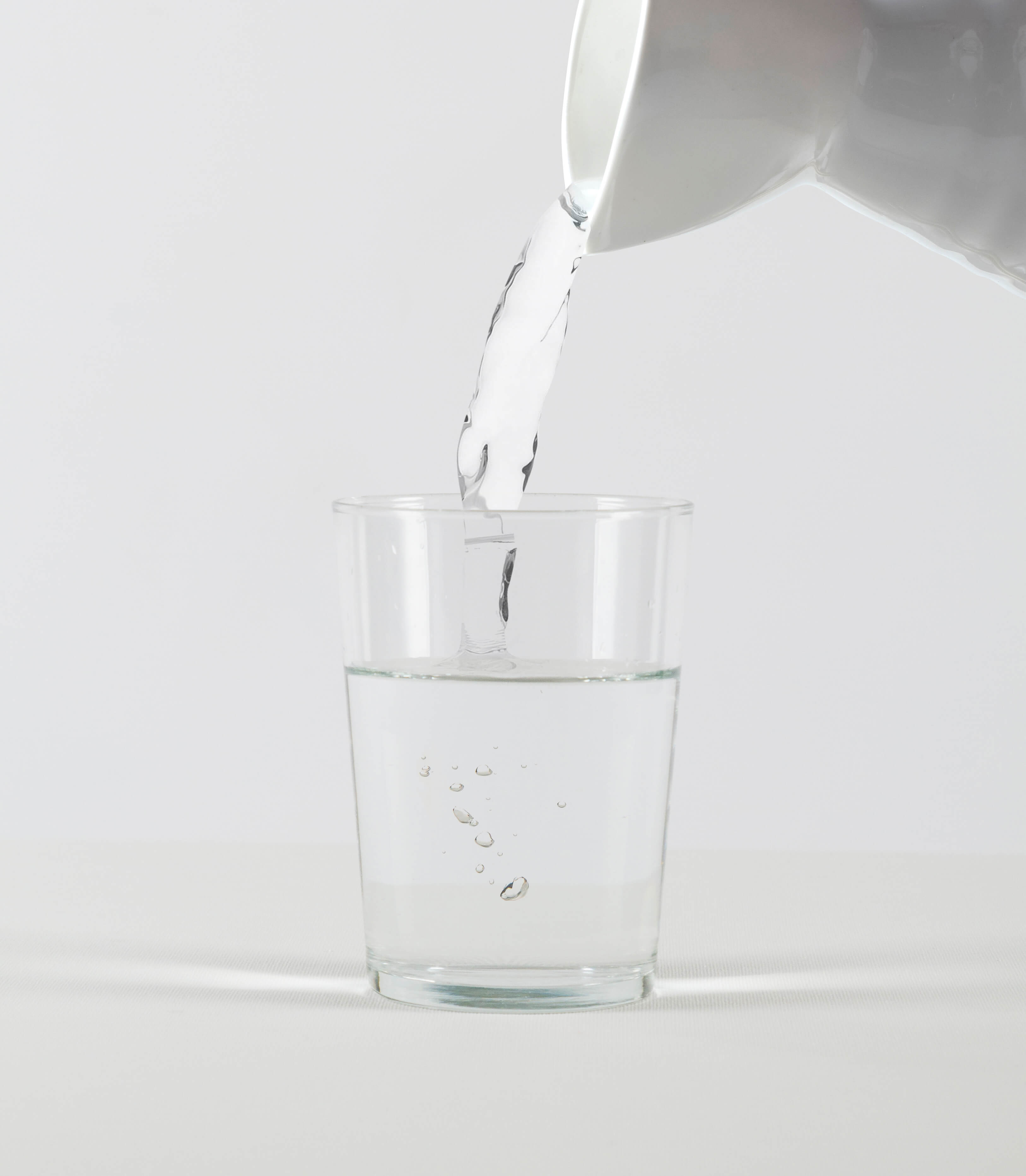A white pitcher pours water into a clear glass against a white background.