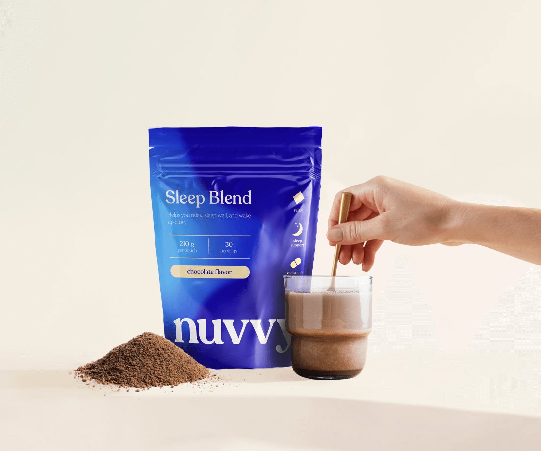 A hand stirs Nuvvy Sleep Blend chocolate powder in a glass next to the pouch and a pile of powder.