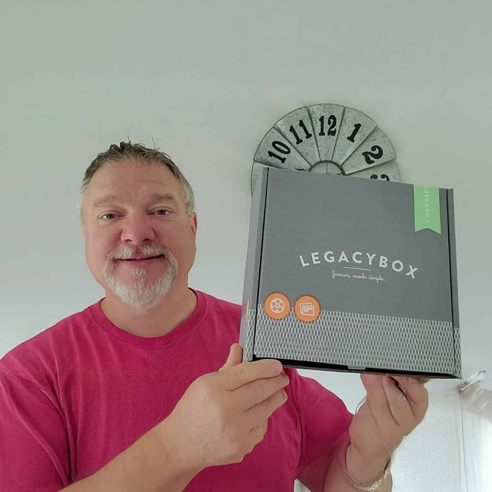 Person holding a Legacybox with a gray wall clock in the background.