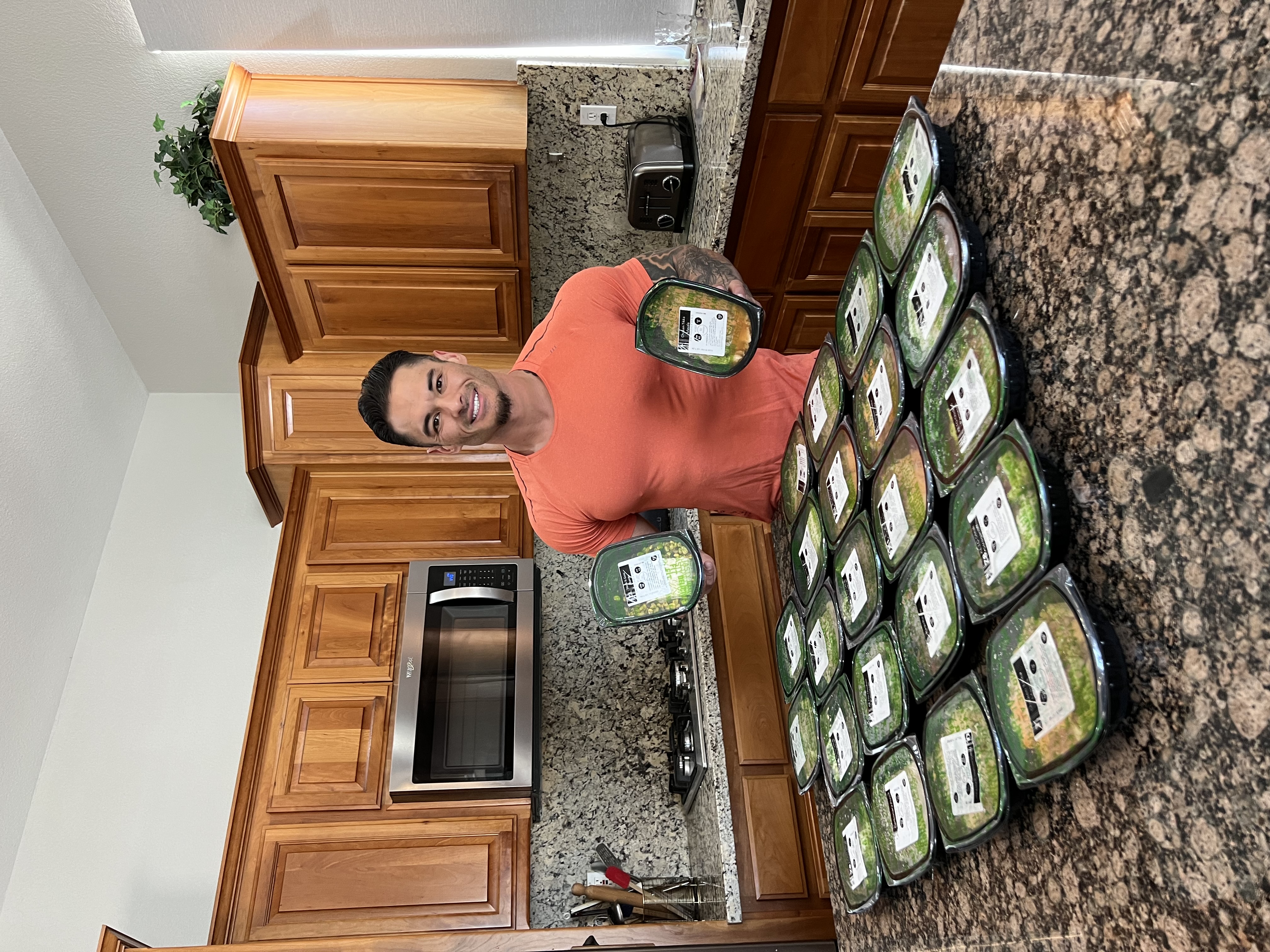 A person in a kitchen holding two prepared meal containers with many more on the counter.