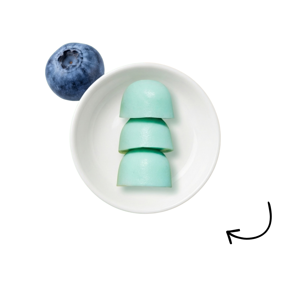 A stack of three light blue, dome-shaped objects in a small white bowl, next to a single blueberry.