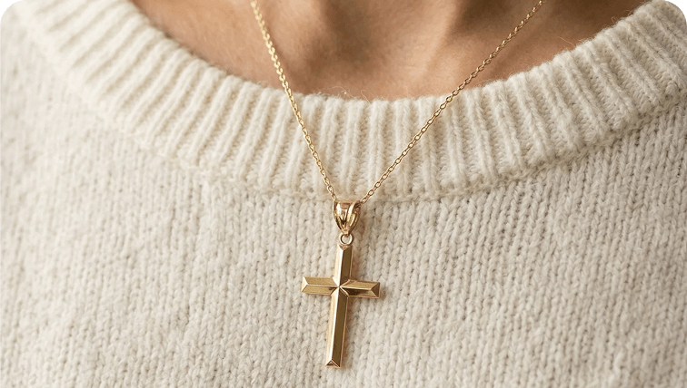 A close-up of a person wearing a gold cross necklace over a cream-colored knit sweater.