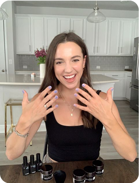 Woman showing her painted nails, sitting at a table with nail products.