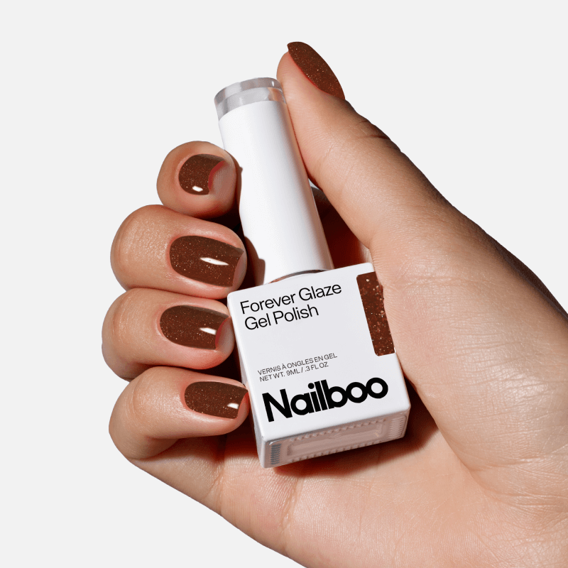 Hand holding a bottle of brown gel nail polish with matching painted nails.