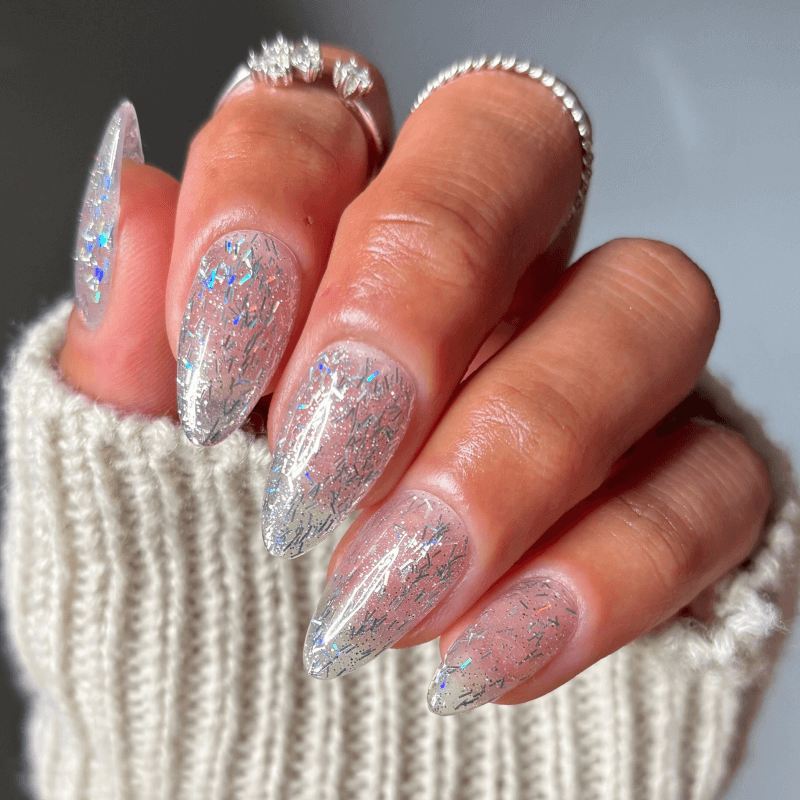 Hand with glittery, silver nail art and rings, wearing a knitted sweater.