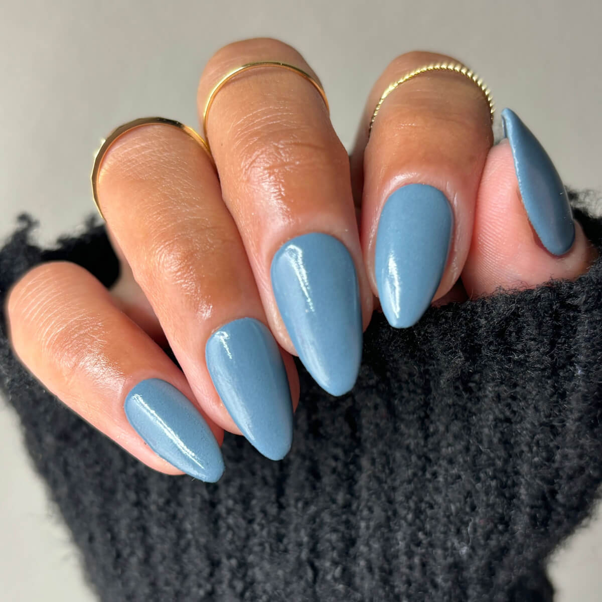 Hand with blue polished nails and gold rings.