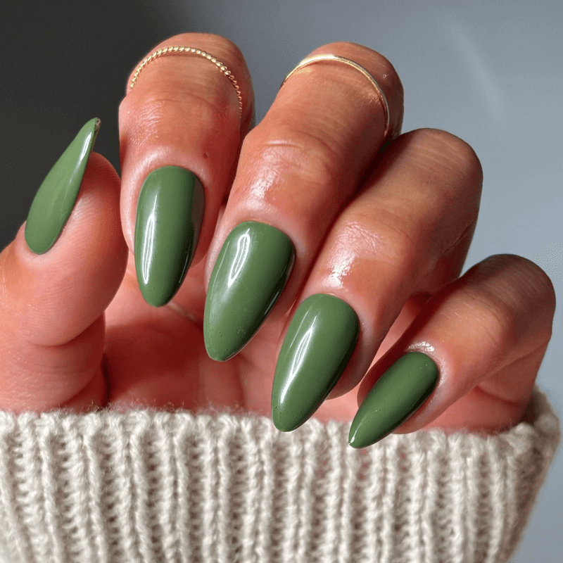 Hand with long, green, almond-shaped nails and gold rings.