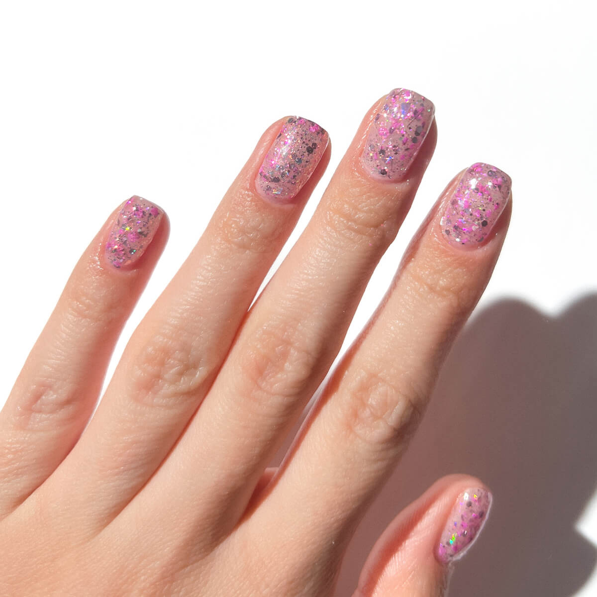 Hand with pink glitter nail polish on short nails.