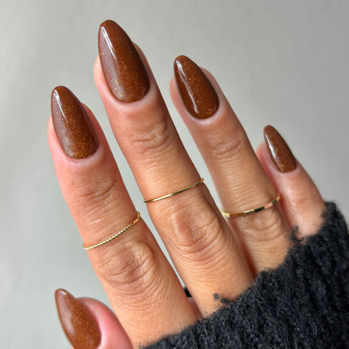 Hand with brown polished nails and gold rings on fingers.