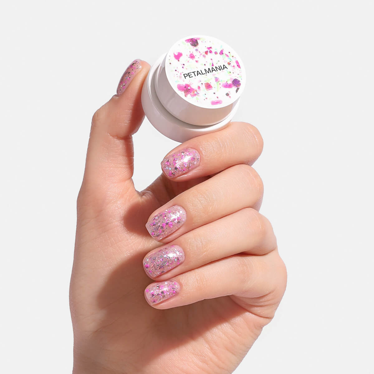 Hand holding a container labeled 'Petalmania' with glittery pink nails.