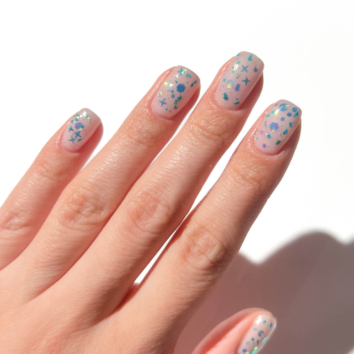 Hand with pastel nail polish and star glitter accents.