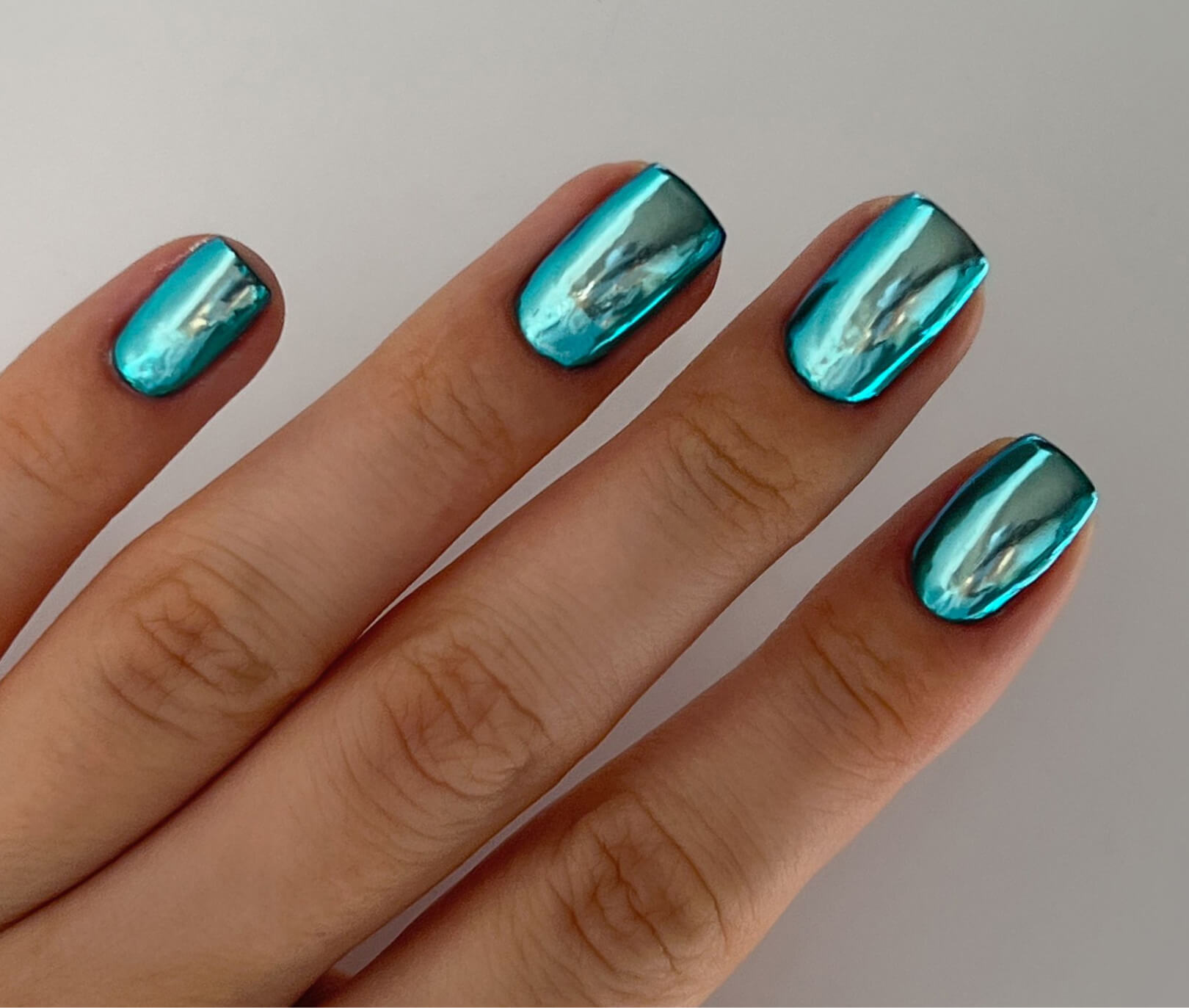 Four fingers with metallic blue nail polish on white background.