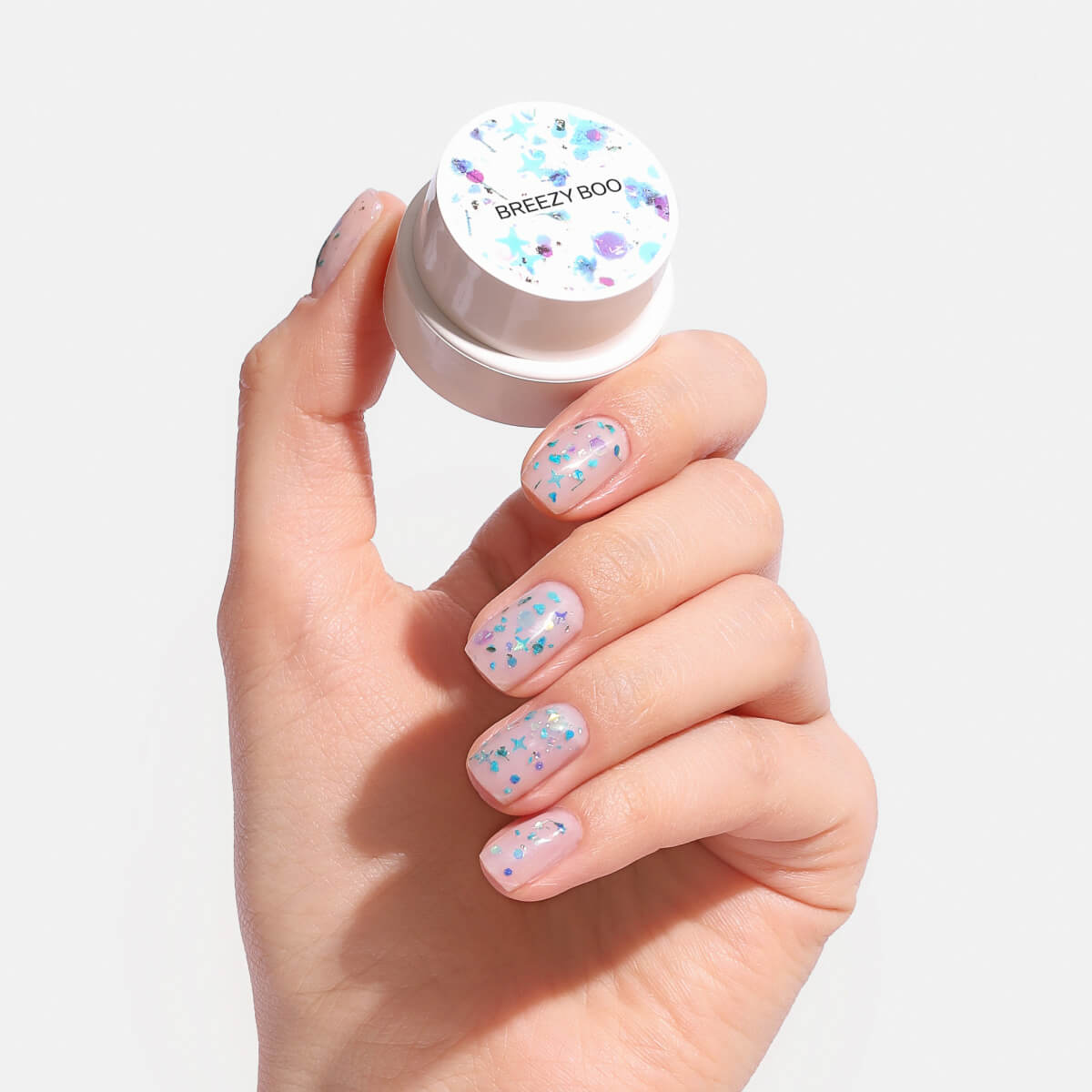 Hand holding a jar with glittery, pastel nail art.