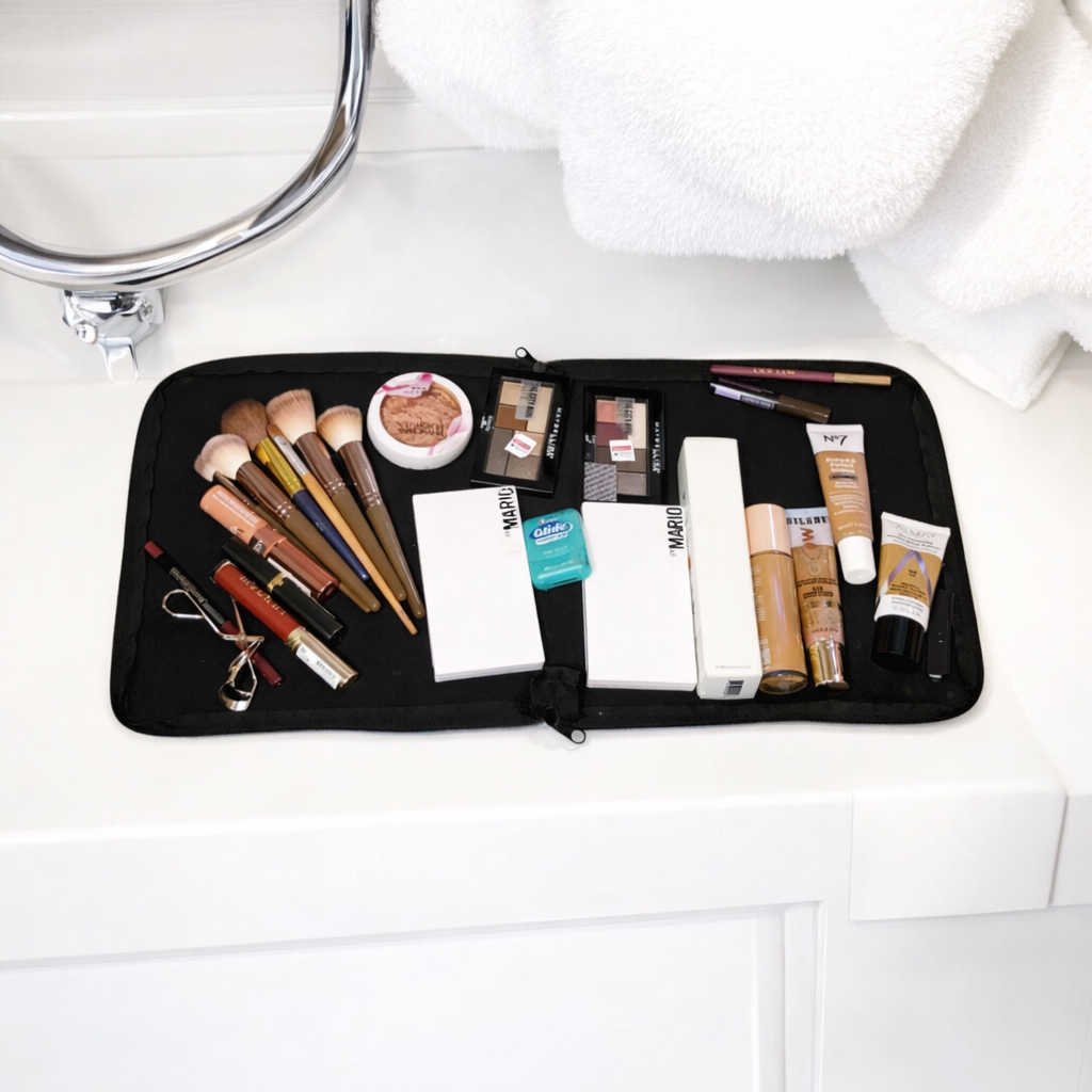 Various makeup products and brushes are laid out on a black mat on a white bathroom counter.
