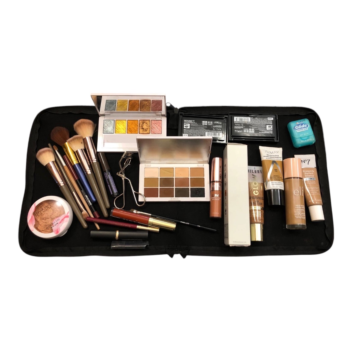 A collection of various makeup products and tools laid out on a black case against a white background.