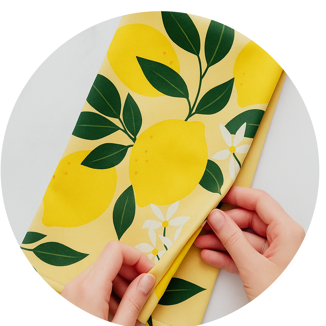 A pair of hands folding a yellow cloth with a lemon and flower pattern.