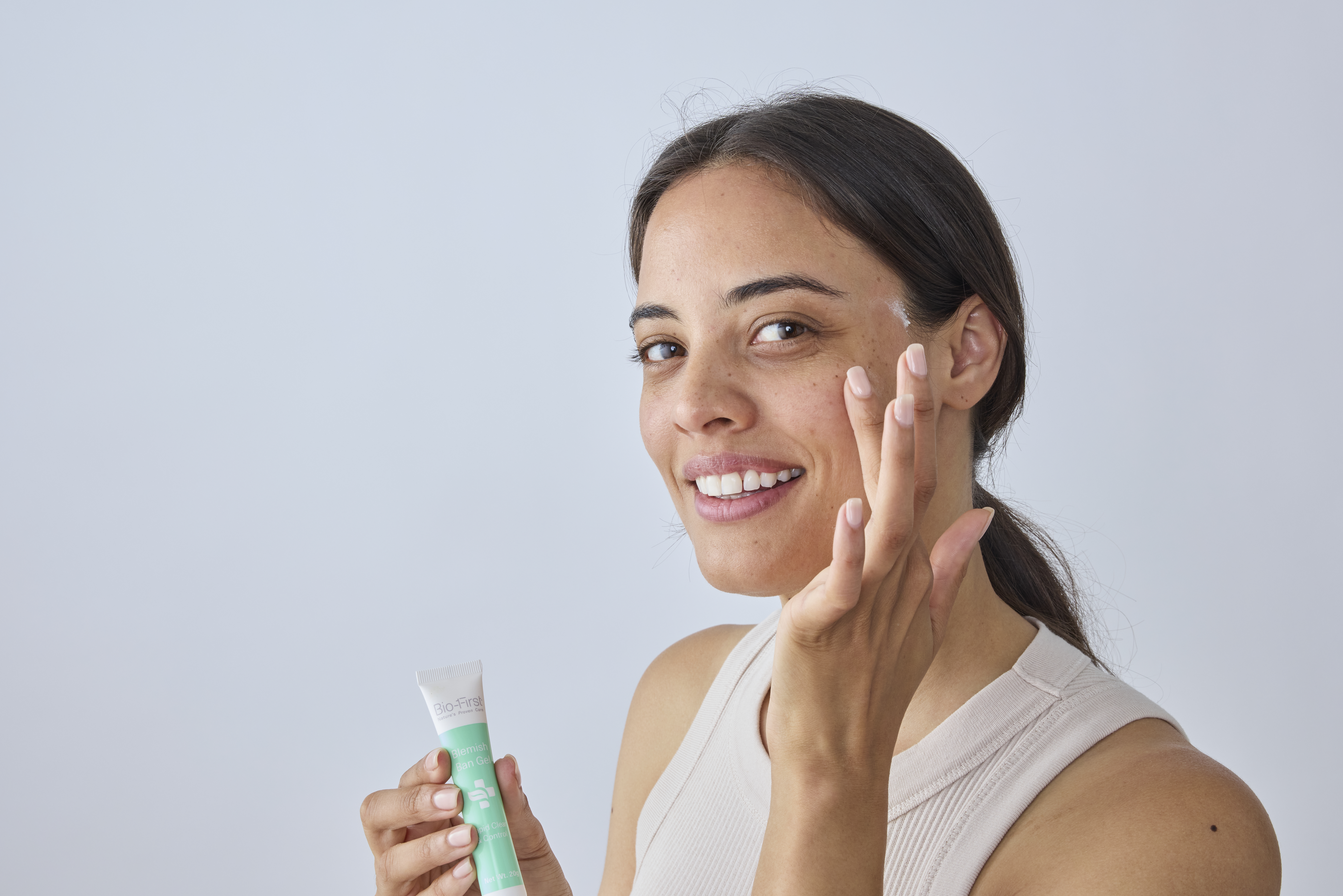 A person applying skincare product to their face, smiling.