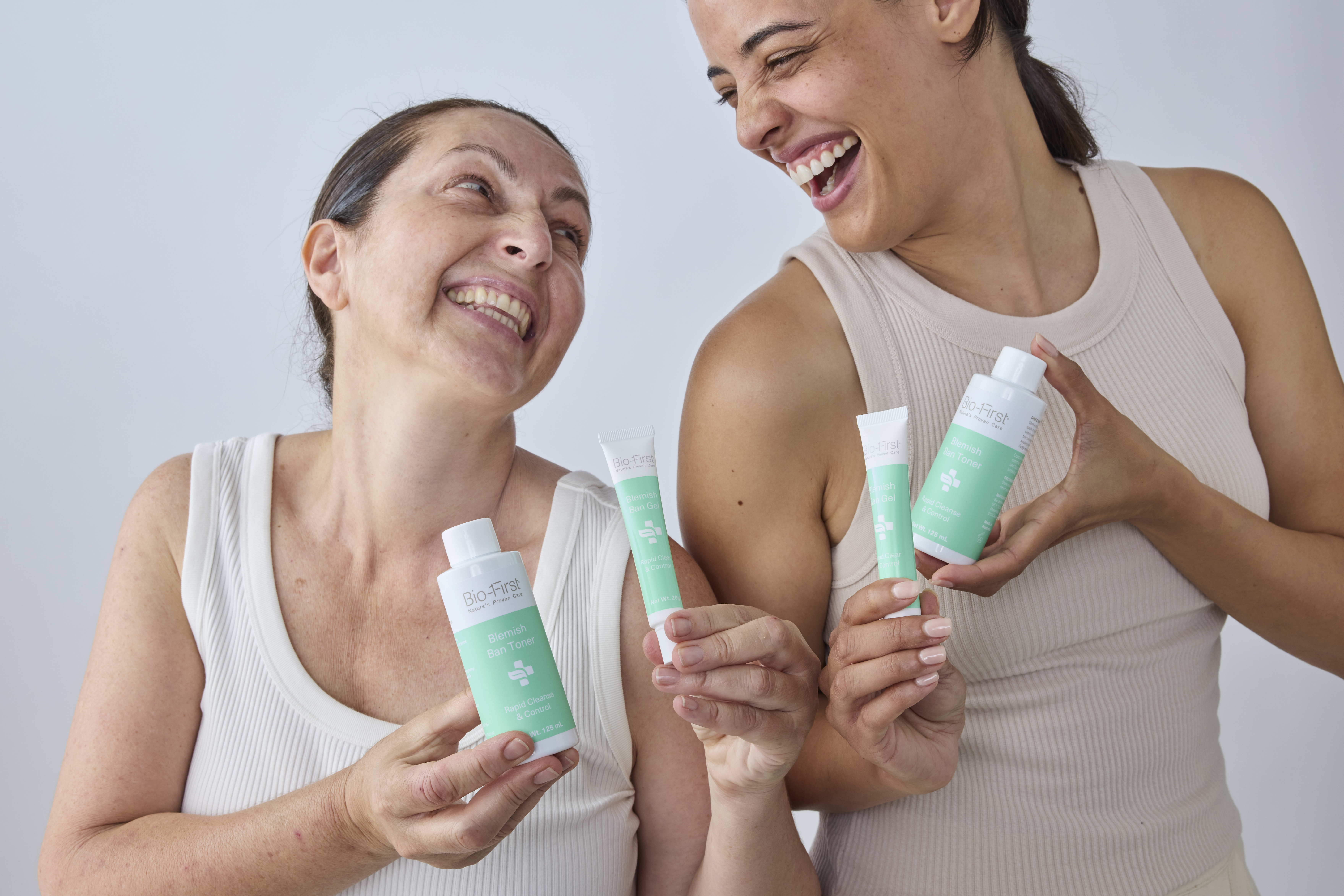 Two smiling women holding Bio-First Blemish Ban skincare products.