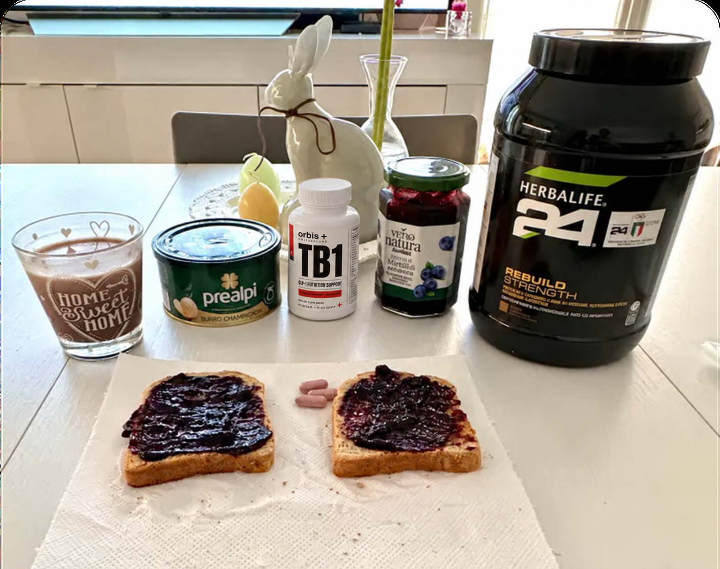 A breakfast of toast with jam, supplements, a protein shake, and a hot beverage on a table.