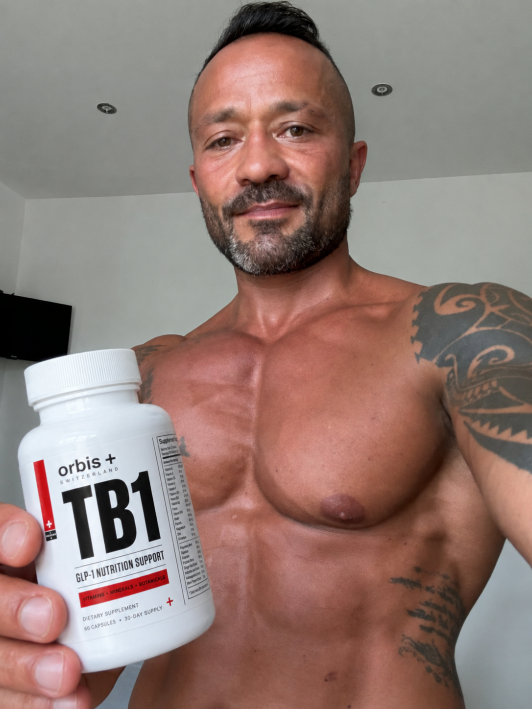 A shirtless, muscular man with tattoos holds up a bottle of Orbis+ TB1 supplements.