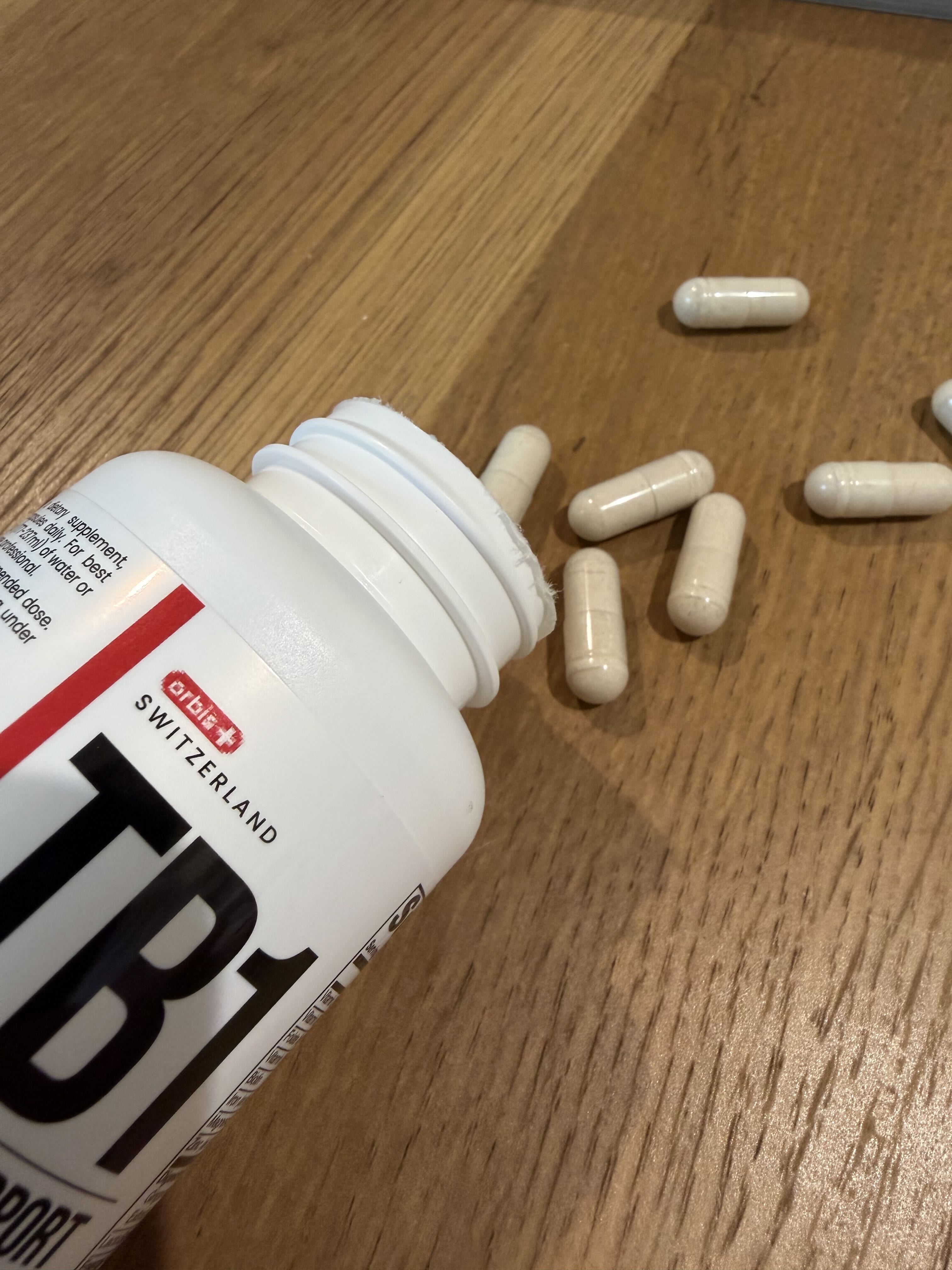 A white supplement bottle has spilled, with several capsules scattered on a wooden surface.
