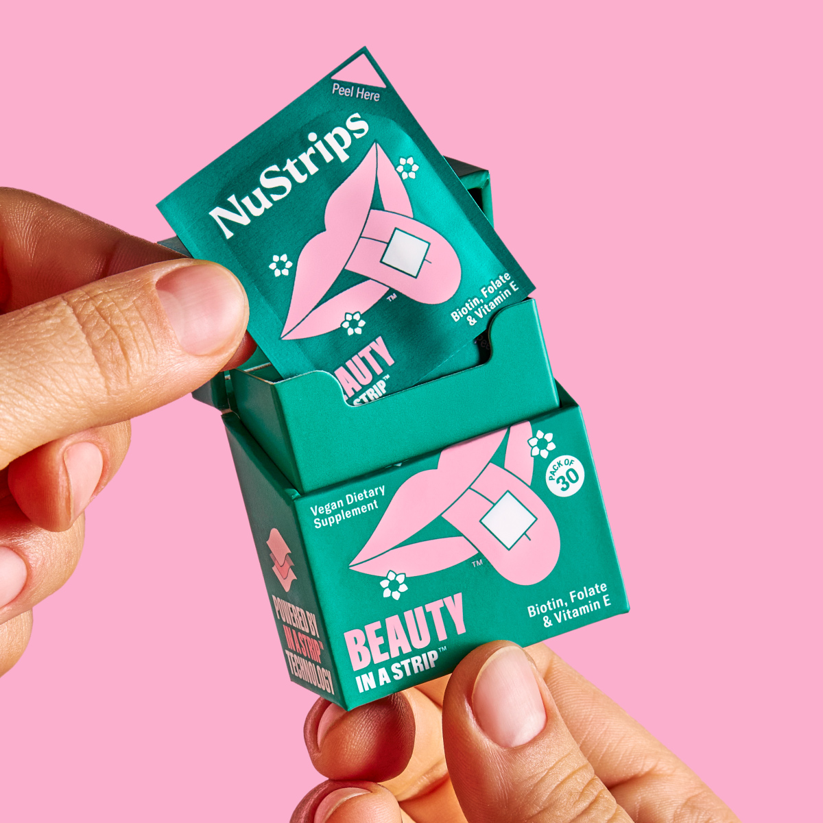Hands holding a green box of NuStrips dietary supplements against a pink background.