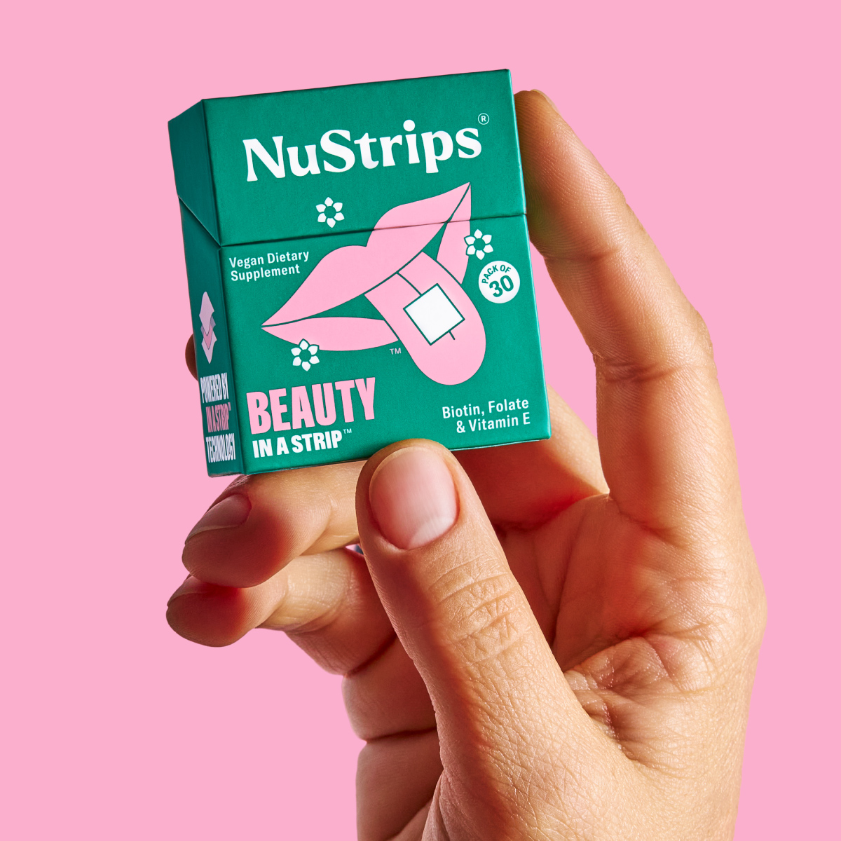 Hand holding a NuStrips beauty supplement box with pink background.