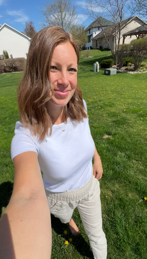 Person taking a selfie in a grassy backyard with houses in the background.