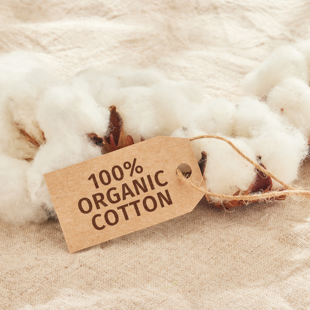 Cotton bolls with a tag reading '100% Organic Cotton' on a fabric background.